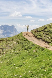 Person hiking on a path with views of rocky mountains and wide skies, Schlehrn hike, Alpe di Siusi,