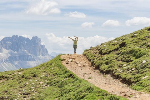 Person spreading his arms on a path in front of a majestic mountain scenery, Schlehrn hike, Alpe di