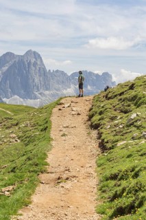 Hiker standing on a path with visible rocks and imposing mountains, Schlehrn hike, Alpe di Siusi,