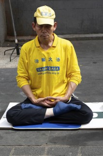 Falun Dafa or Falun Gong man meditating sitting cross legged, Gerrard Street, Chinatown, West End,