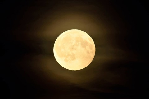 Round, full moon, bright shining full moon in starry night with a small aura caused by thin clouds,