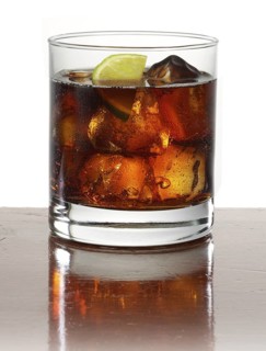 Cocktail in a tumbler on ice with half a slice of lime as garnish against a white background,