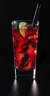 Cocktail in a long drink glass on ice with a slice of lime and as a garnish in front of a black