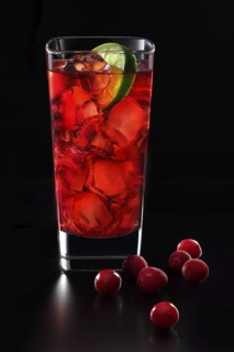 Cocktail in a long drink glass on ice with a slice of lime and cranberries as garnish against a