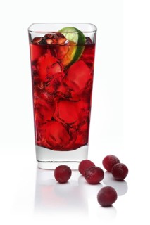 Cocktail in a long drink glass on ice with a slice of lime and cranberries as garnish against a