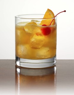 Cocktail in a tumbler on ice with half an orange slice and cocktail cherry as garnish against a