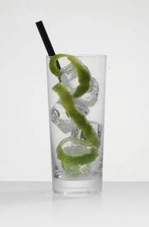 Betautes cocktail glass, filled with ice cube cubes, lime zest as garnish, in front of a white