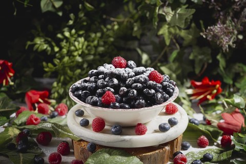 Blueberries and raspberries with icing sugar in a bowl, decoratively arranged, surrounded by leaves