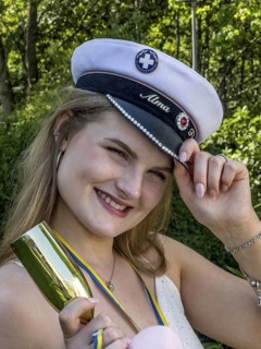 Happy blonde student on graduation day, holding her cap and smiling at the camera, in Ystad, SkÃ¥ne
