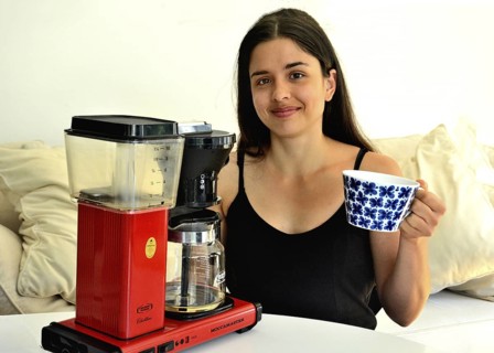 Young beautiful Southern European woman, brunette, 30 years old, demonstrating a coffee machine in