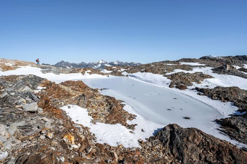Mountaineer in rocky high mountain landscape, frozen small mountain lake, mountain tour from the