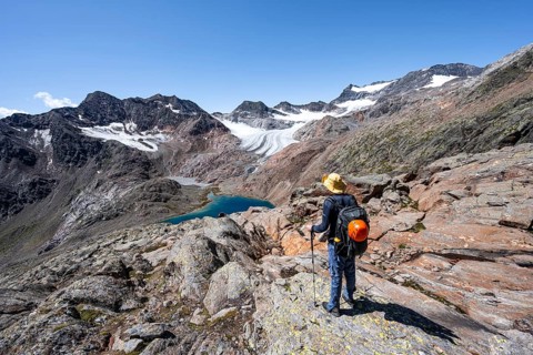 Mountaineer on hiking trail, view of blue glacial lake in rocky mountain landscape, behind