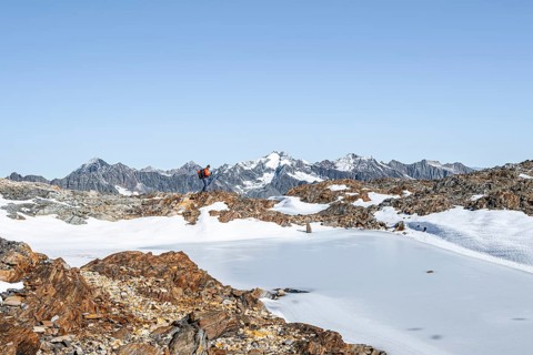 Mountaineer in rocky high mountain landscape, frozen small mountain lake, behind mountain peak