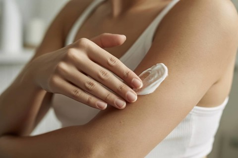 Close-up of woman applying moisturizing cream to arm. Concept for skincare and self-care routine.