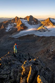 Mountaineer in front of picturesque high mountain landscape at sunrise with alpenglow, glacier and