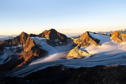 Picturesque high mountain landscape at sunrise with alpenglow, glacier and rocky mountain peaks in