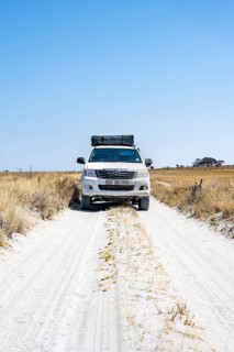 Off-road vehicle driving on a sandy track between yellow dry grass, Makgadikgadi salt pans,