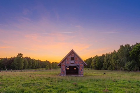 View of an open half-timbered barn standing on a pasture in the sunset, meadow, spring, awakening,