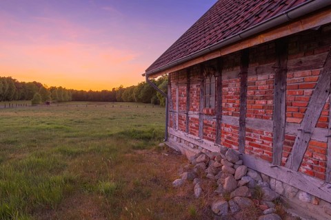 View along an outer wall of a half-timbered barn standing on a pasture in the sunset, meadow,