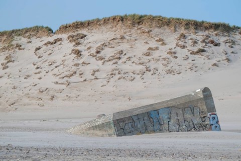 Abandoned bunker from the 2nd World War, sunken into the sand with graffiti, surrounded by sand
