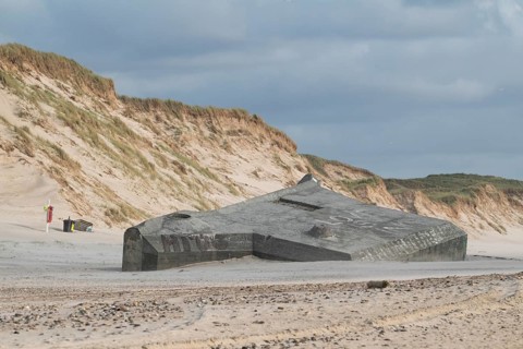 Abandoned bunker from the 2nd World War, sunken into the sand with graffiti, surrounded by sand