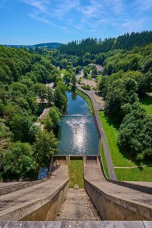 A high view of a dam with a river and lots of greenery all around under a clear sky, Oleftalsperre,