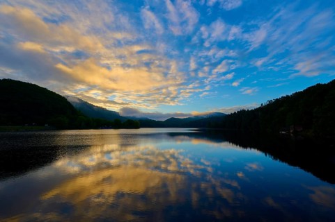 Atmospheric morning mood at the lake with reflecting sky in calm water and surrounding mountains,