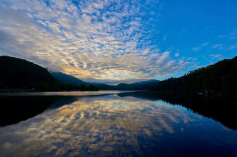 Peaceful morning atmosphere with dramatic sky reflected on the still lake, surrounded by green