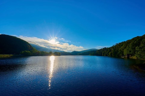 Lake in the morning light with sun, blue sky and surrounding mountains, summer, Rursee, Obersee,