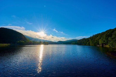 The sunny morning mood is reflected golden on the water of the lake, surrounded by peaceful hills
