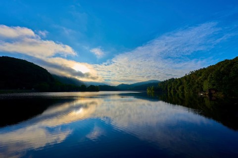 A tranquil lake reflecting dramatic sky and clouds offers a calming view with sweeping mountains,