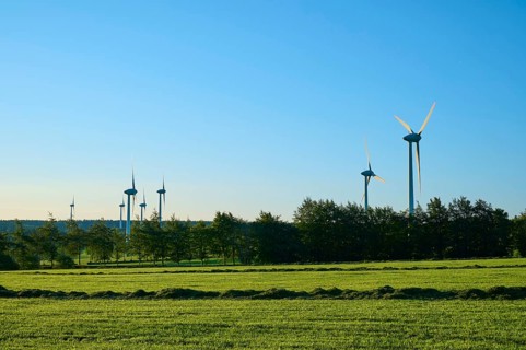 Wind turbines stand on a green meadow under a blue sky, surrounded by trees, summer, pipes,