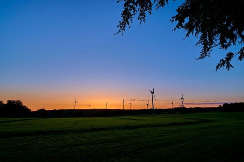 Silhouettes of wind turbines rise into the colourful morning sky as the sun rises behind the