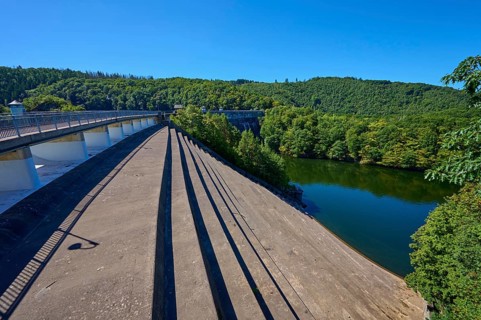 View of a large dam with dense forest under a clear blue sky, summer, Urft dam wall, Obersee,