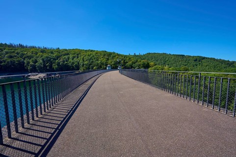 Straight view of an asphalted bridge with railing over a dam, summer, Urft dam wall, Obersee,