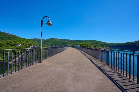 Asphalted bridge with railing over a water reservoir under a blue sky, summer, Urft dam, Obersee,