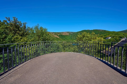 Viewing platform with railings in front of a wooded hilly landscape under a clear blue sky, summer,