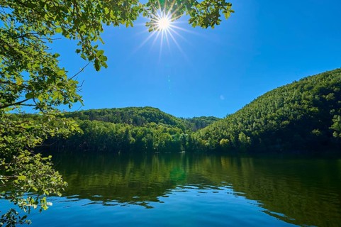 Clear lake landscape with bright sun in the blue sky, surrounded by lush green forests, summer,