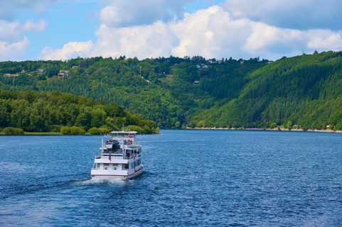 A passenger ship, stern view, sailing across a wide lake, surrounded by green hills, summer,