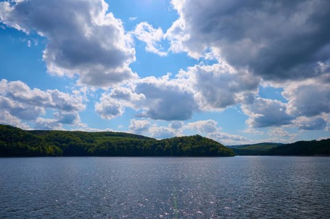 Blue sky with clouds over a calm, glittering lake and wooded hills, summer, Rursee, Rurtalsperre,