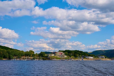 Buildings and boats along a lake in front of a sky with white clouds, summer, Rursee, Rurtalsperre,