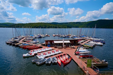 Pedal boats and other boats are moored on a jetty in a large lake and offer leisure activities,