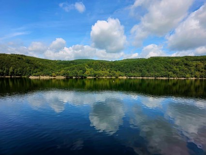 Clear blue sky with white clouds reflected in the still water of a lake and wooded shores, summer,