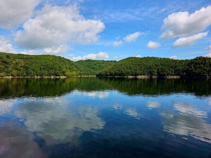 Blue sky with white clouds and their reflection in a calm lake, surrounded by lush forests, summer,