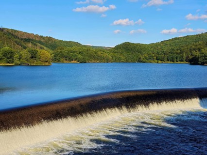 Clear water flows over a dam in a lake surrounded by forests with a blue sky, summer, Rursee,