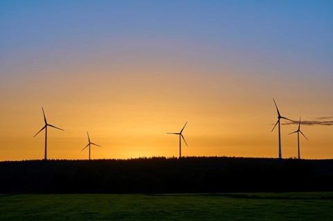 Wind turbines in front of an orange-coloured sky at sunrise, above a meadow, summer, Rohren,