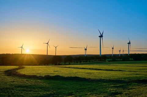 Series of wind turbines at sunrise, play of lights on a green meadow, summer, Rohren, Monschau,