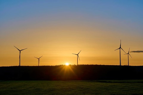 Sun rises behind a row of wind turbines and illuminates the sky orange, summer, Rohren, Monschau,
