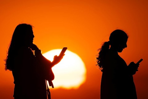 People photographing the sun setting on the horizon with their smartphones from the summit of the