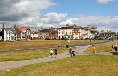 People walking on paths on grass area next to Queens Road, Southwold, Suffolk, England, Uk